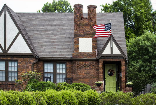 Charming brick house with landscaping and lime green door with wreath and American flag flying with lush trees behind