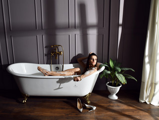 Young beautiful woman sitting in bathroom near expensive bathtub bath looking at the corner on dark 