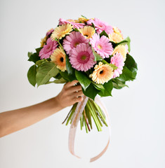 Beautiful woman hands hold bouquet of gerbera flowers pink and yellow on grey