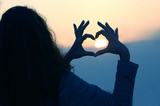 The girl shows her hands the sign of the heart against the setting sun