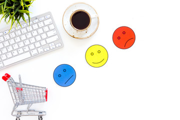 Client feedback concept. Emoji smiling, neutral, sad face near shopping cart on work desk on white background top view space for text