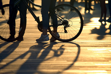 Fototapeta na wymiar Feet with bike and people behind the setting sun