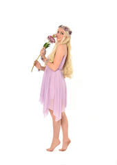 full length portrait of blonde fairy girl, holding flowers. standing pose on white studio background.