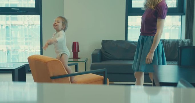 Toddler climbing on furniture with his mother watching