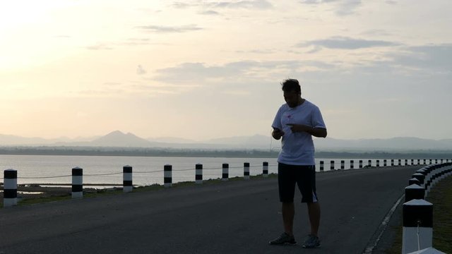 Men use a Smartphone taking pictures of yourself and running in the time during sunrise on dam road exercise. Living healthy lifestyle concept. 