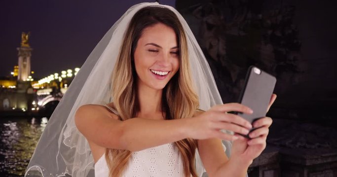 Joyful bride taking a selfie in Paris at night, Beautiful Caucasian woman taking a picture in her wedding dress and veil, 4k