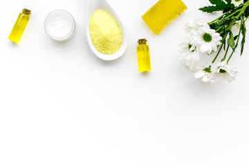 Chamomile spa cosmetics with natural herbal ingredients. Chamomile spa salt, soap, oil and cream on white background top view copy space