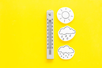Weather forecast concept. Air temperature. Termometer among cloud, sun, rainy clouds, snow on yellow and yellow background top view copy space