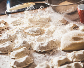Hands sprinkle with flour raw dumplings on table