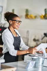 friendly african american shop assistant using pos terminal to input orders at restaurant