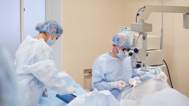 Male surgeon and female assistant during an operation. Assitant putting instruments on a table. Modern equipment.