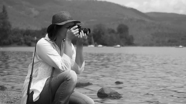 Happy beautiful woman hobby photographer taking pictures of nature in front of sea black and white