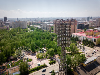 Aerial photography of a modern city park with green trees, attractions, high-rise buildings, roads with cars on a warm summer day. Helicopter drone shot