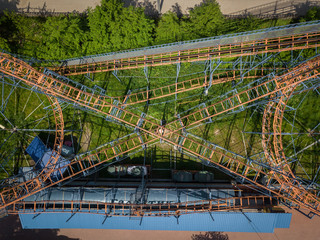 Aerial photography of a children's orange roller coaster with loops and rises in the hill in the city park   on a warm summer day. Helicopter drone shot