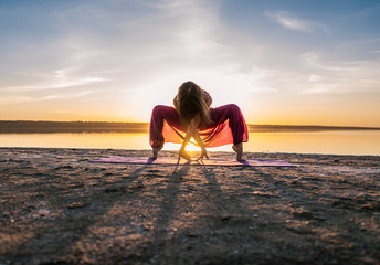 woman on the beach at sunset starts doing yoga asana training . Morning natural stretch warm-up training