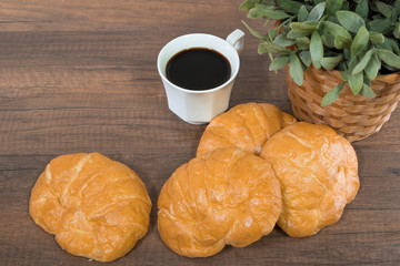 Freshly baked homemade croissants and black coffee on wooden cutting board, top view