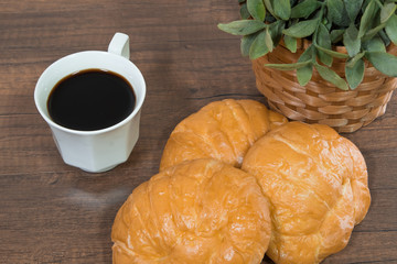 Freshly baked homemade croissants and black coffee on wooden cutting board, top view