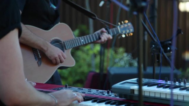 Music band playing on keyboards and guitar outdoors event wedding active sound back side close up view. Two unrecognizable musicians perform electronic instruments slow motion live concert inspiration