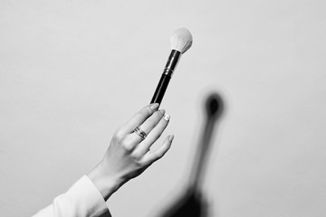 Closeup of female hand holding makeup brushes against pink background. Hard lightining with shade