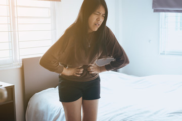 Asian woman having painful stomachache in bedroom after wake up,Female suffering from abdominal...
