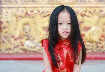 Happy little Asian girl in Cheongsam respecting on traditional Chinese new year festival on Chinese background.
