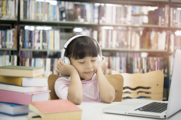 Cute asian little girl reading a book and headphones listening to music, 