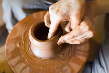 Rotating potter's wheel and clay ware on it taken from above. Hands in clay. Pottery male ceramist creates a hand made clay product. Process of rotation of potter's wheel, hands of ceramist