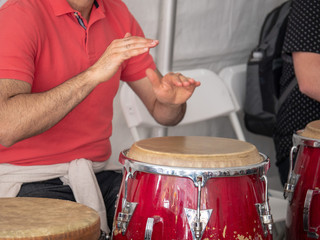 Man beats on red conga drum with bare hands with crowd