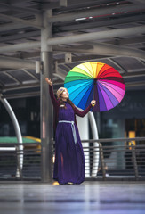Asian girls standing and smiling in purple dress holding colorful umbrellas after rain.