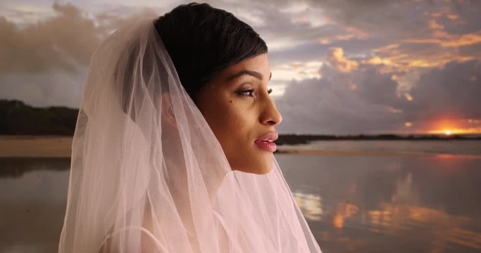Side view of gorgeous bride on the beach, joyful and excited, Black woman in cute elegant dress with veil getting married, sunset outside, 4k