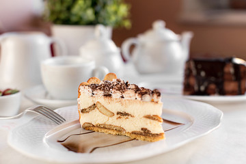 Slice of delicious cake tiramisu with cream decorating with chocolate serving on plate on table with different porcelain in cafe
