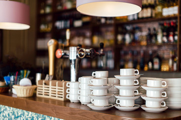 Stacked and prepared ceramic cups with saucers placed on wooden counter of a bar