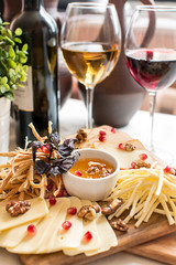 Crop glasses with white and red wine serving with different kinds of tasty cheese on board