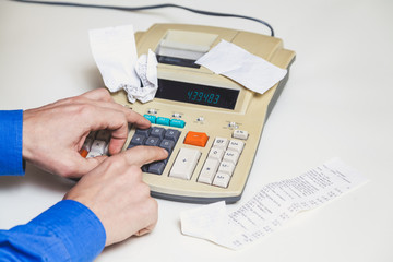 Hands press keys on printing calculator beside lie checks