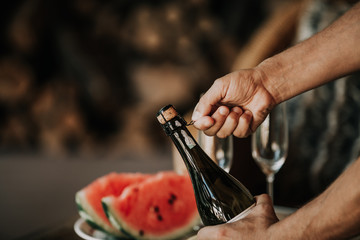 Hands open bottle of champagne. Back watermelon and fruit