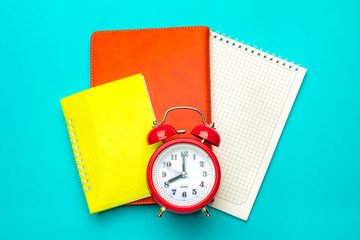 Stationary, back to school,college,summer time, creativity and education concept.School supplies-notepad, calendar,red alarm clock on blue background,flatlay.Mock up.Top view.Copy space