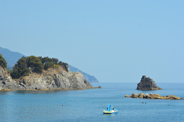 Fototapeta premium A paddle boat in a bay surrounded by rocks. A headland is covered by trees. The sky is clear.