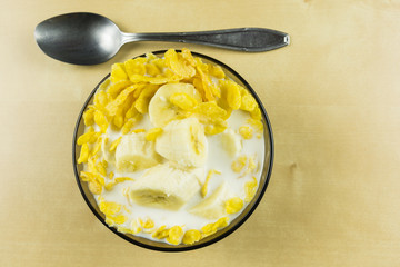 Top view of a bowl of cornflakes with cold milk and banana.