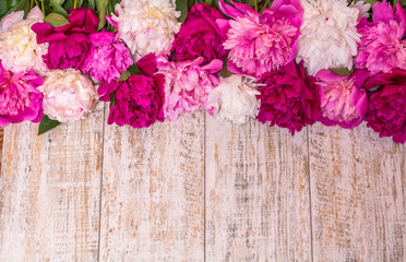 Border of peonies on a wooden background with empty space for text. Floral design. Pink and purple spring flowers.