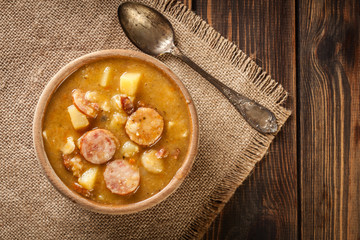 Wooden bowl of split pea soup with sausage and potatoes