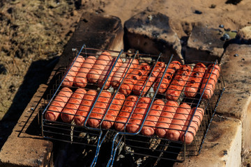 Grilling sausages in barbecue grill cooking on campfire