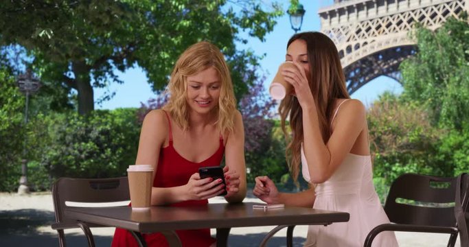 Portrait of two lovely young women looking at cellphone in summer dresses in front Eiffel Tower in Paris, France, Couple of cute girls sharing smart phone by famous French monument, 4k