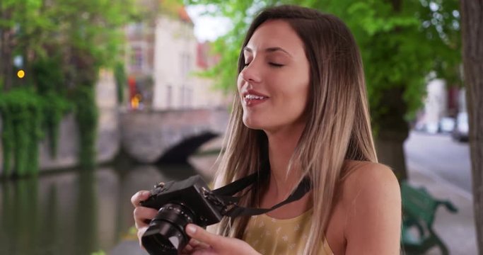 Happy Caucasian woman with camera taking photos while exploring city of Bruges, Brunette millennial in her 20s shooting pictures with camera while on vacation in Bruges, Belgium, 4k