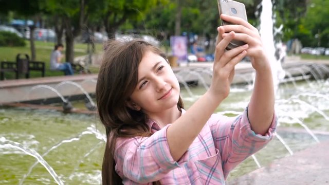 Attractive girls are taking selfie with their cell phone. Brunettes are smiling and look very happy. Outdoors.