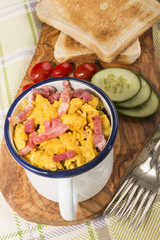 scrambled eggs with roasted bacon in an enamel mug
