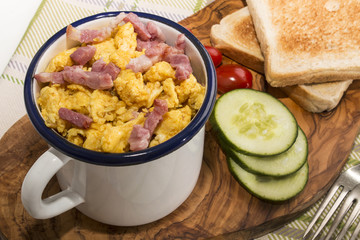 scrambled eggs with roasted bacon in an enamel mug