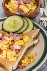 scrambled eggs with fried bacon, toasted bread and sliced cucumber