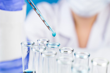 Sientist with pipette blue water drop in test tubes in laboratory.