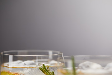 partial view of two glasses of lemonade with pineapple pieces, ice cubes and rosemary on grey background