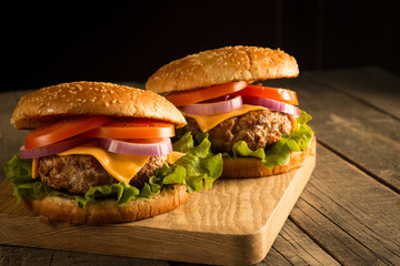Home made hamburger with beef, onion, tomato, lettuce and cheese. Fresh burger close up on wooden rustic table with potato fries, beer and chips. Cheeseburger.
